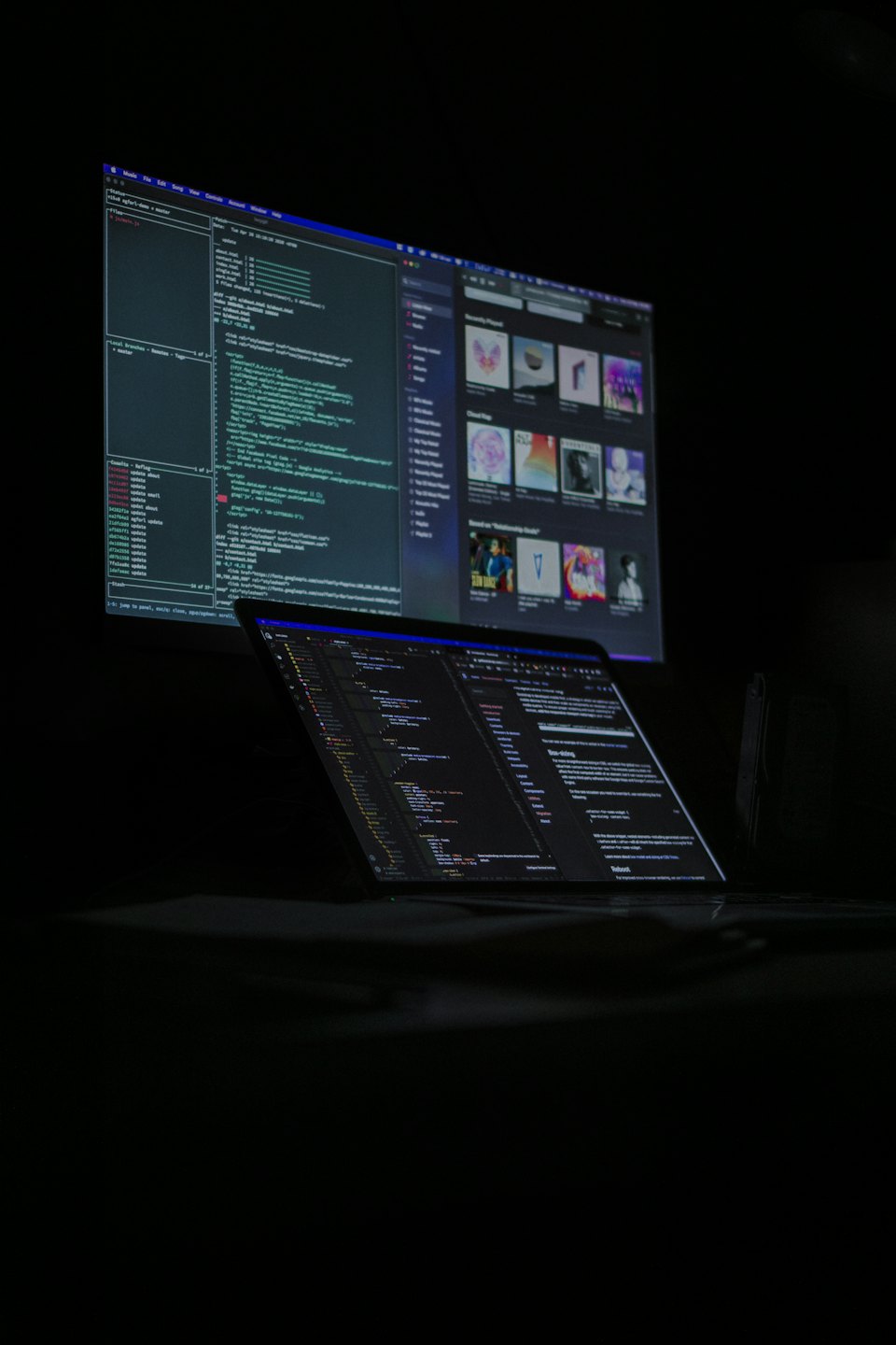 Laptop e monitor che mostrano codice complesso in una stanza buia.
